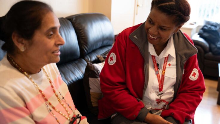 A British Red Cross health worker sits with a woman on a sofa in our health care film