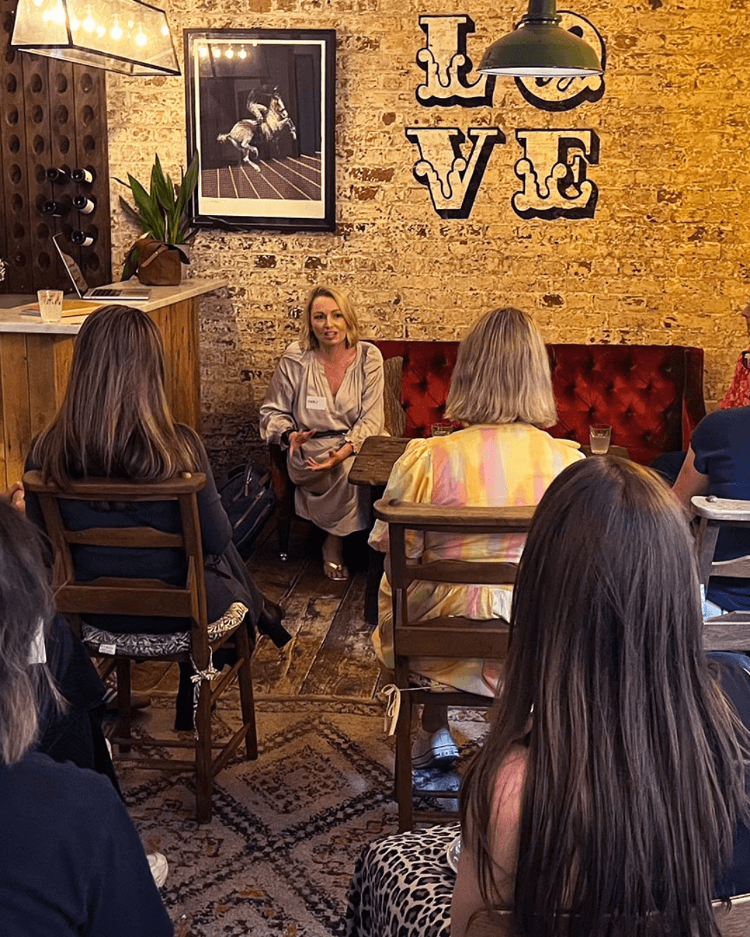 Our guests were spellbound by guest Mary Kemp speaking about AI. The image shows a group of women sitting in rows facing a blond woman in a beige dress, she is talking to the audience animatedly
