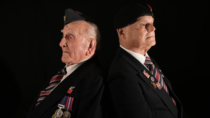 Remembrance Campaign featured image 1 shows two veterans sitting back to back, they are in full uniform with berets and their medals.