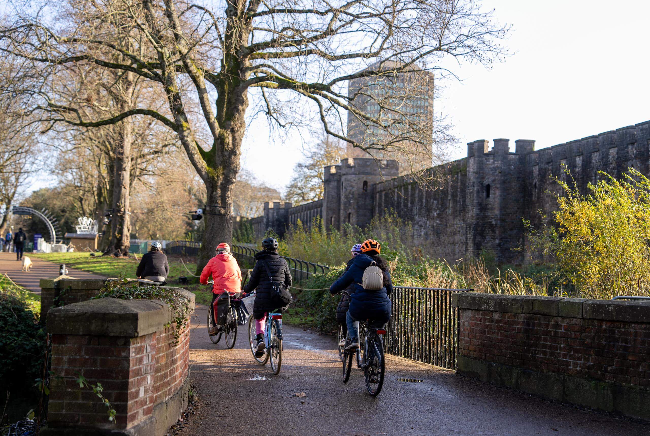 Three cyclists going through the park past Cardiff castle on a sunny autumn day