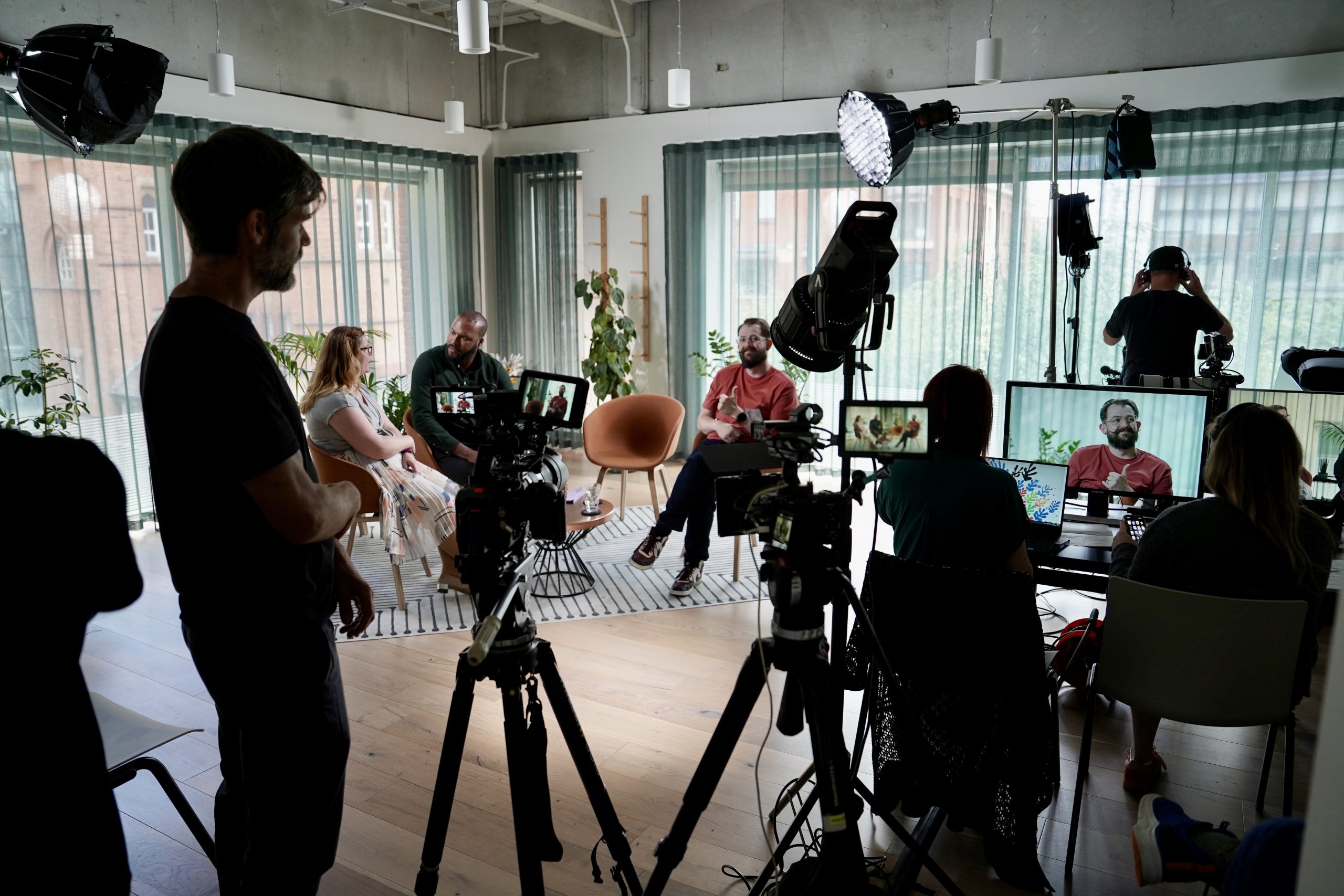Behind-the-scenes filming of a video podcast, with speakers seated in a studio and cameras and lights set up around them.